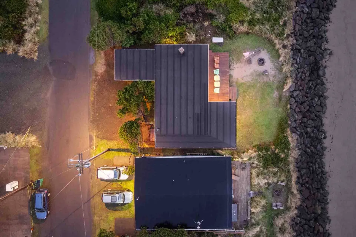 This image captures the house's backyard and its direct connection to the beach, showcasing an inviting outdoor seating area, a pathway, surrounding greenery, and the sandy beach area beyond. It suggests ample space for pets to play and easy access for family beach outings.