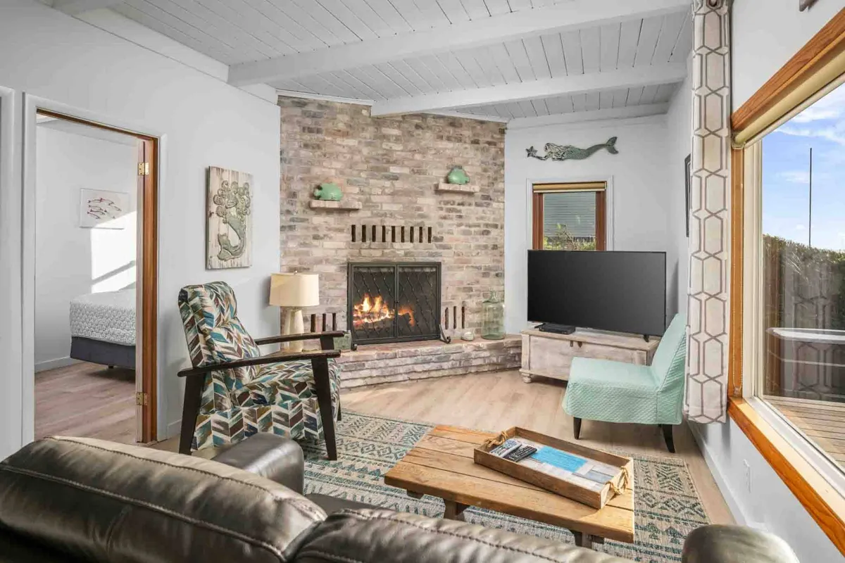 A cozy living room scene showcasing a retro-style fireplace, a large window with an ocean view, a television for movie nights, and carefully curated decorative art pieces. The plush seating invites relaxation and togetherness.