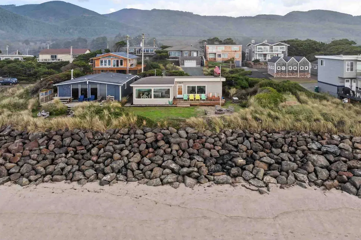 A peaceful exterior view capturing beachfront houses nestled along a wide, sandy shoreline with the ocean and a backdrop of distant mountains. The scene highlights easy beach access and a tranquil setting, perfect for morning walks and sunset relaxation.