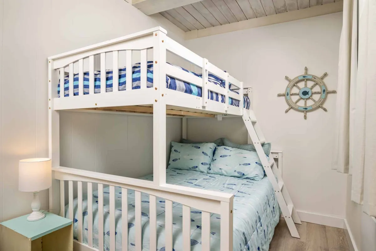 A playful yet peaceful bedroom with a twin bunk bed, nautical decor including a ship wheel, and soft bedding. The room evokes a sense of fun for younger guests while still maintaining a calming atmosphere.
