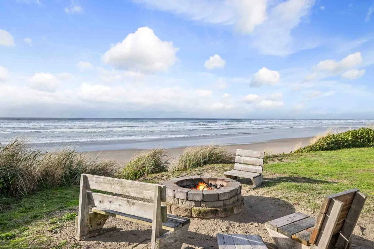 An inviting fire pit on the beachfront, with comfortable seating arranged for couples to relax and take in the expansive ocean and sky. The gentle glow from the fire complements the soft light of dusk, creating an intimate setting for stargazing or sharing a quiet moment by the sea.