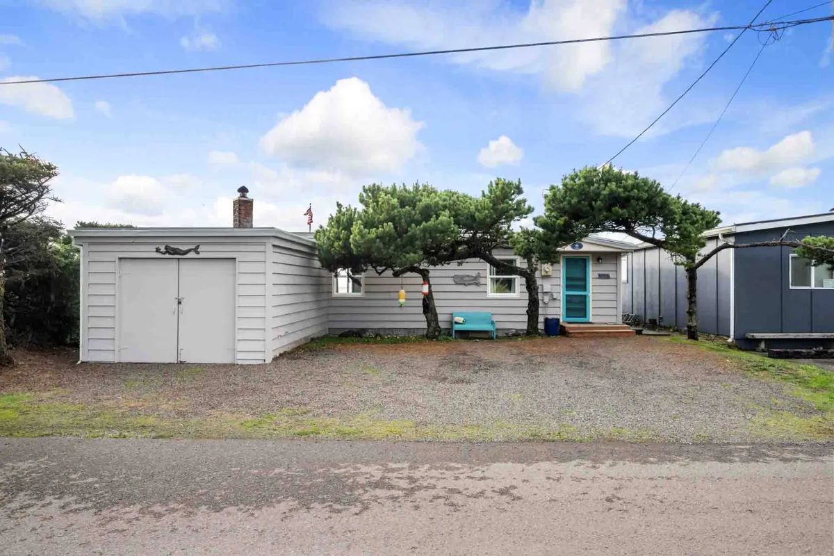 The photo highlights the front of the house with its distinctive teal-colored door, garage, and the surrounding pine trees. While focused on the entryway, it subtly hints at practicality and the presence of amenities like parking.